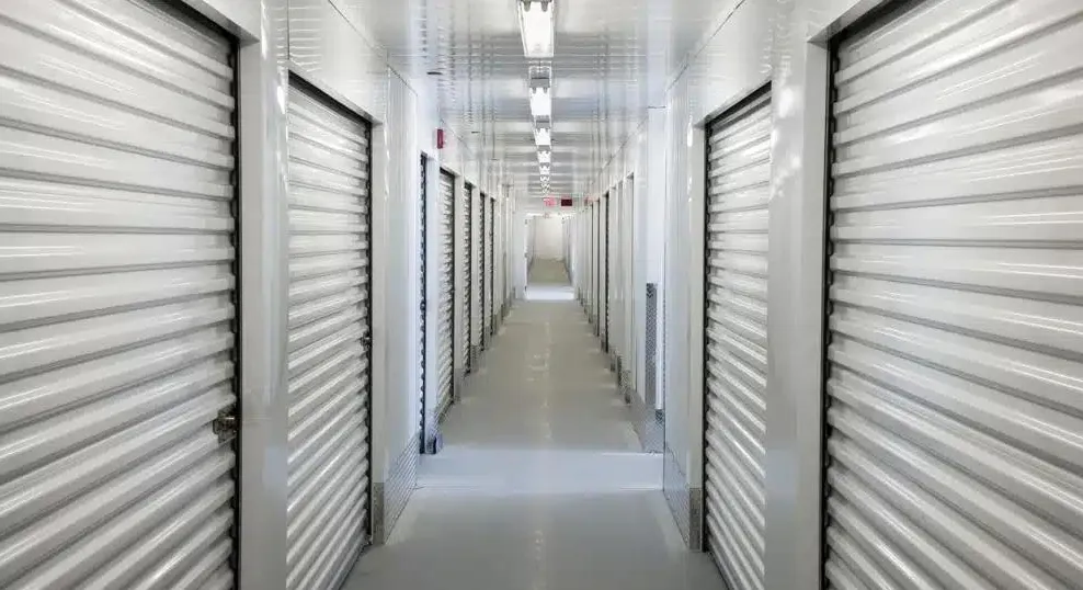 An interior hallway of white climate-controlled storage units receding towards a lit exit.